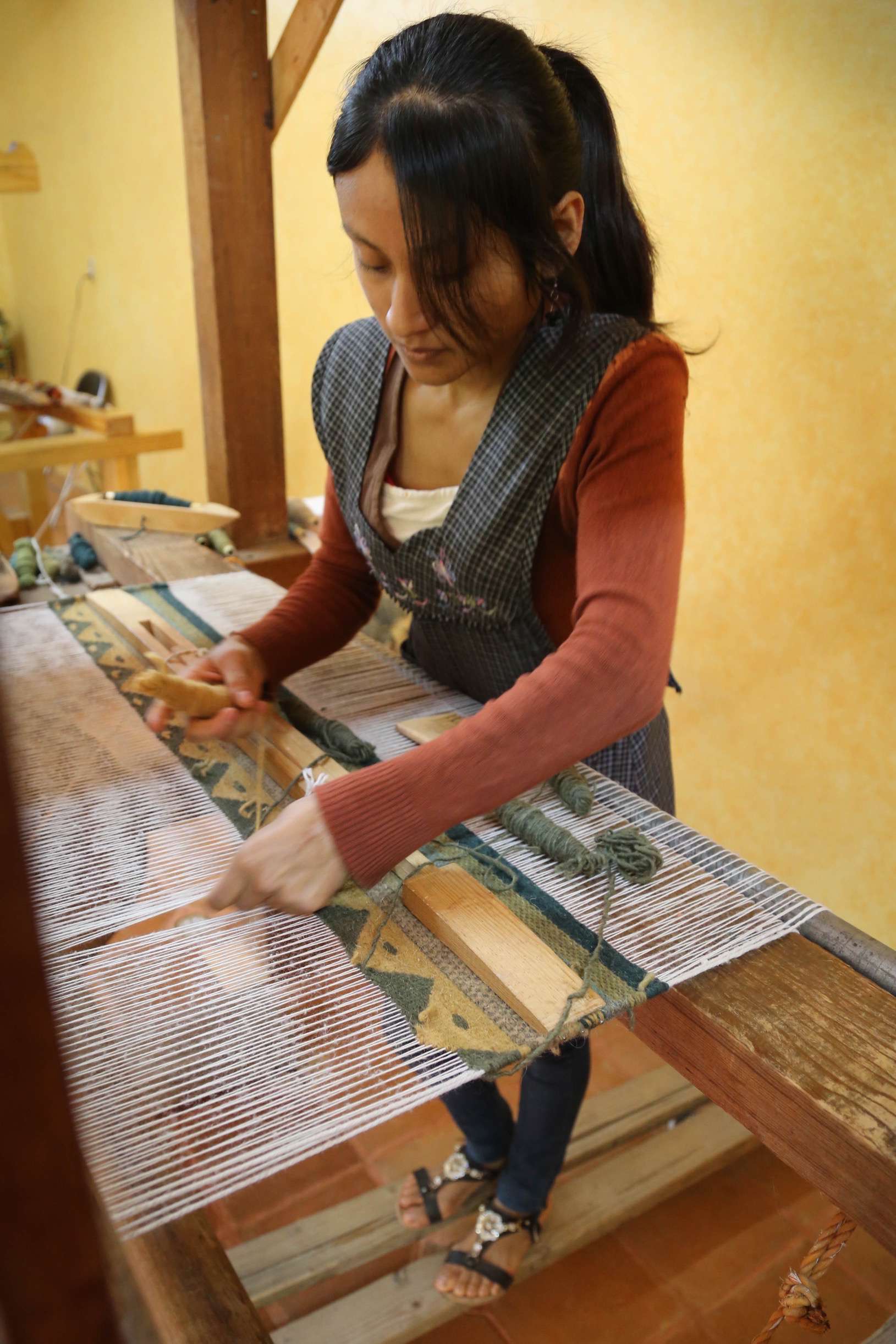 This young woman works on a step loom, carefully following the pattern that has been laid out on the warp.